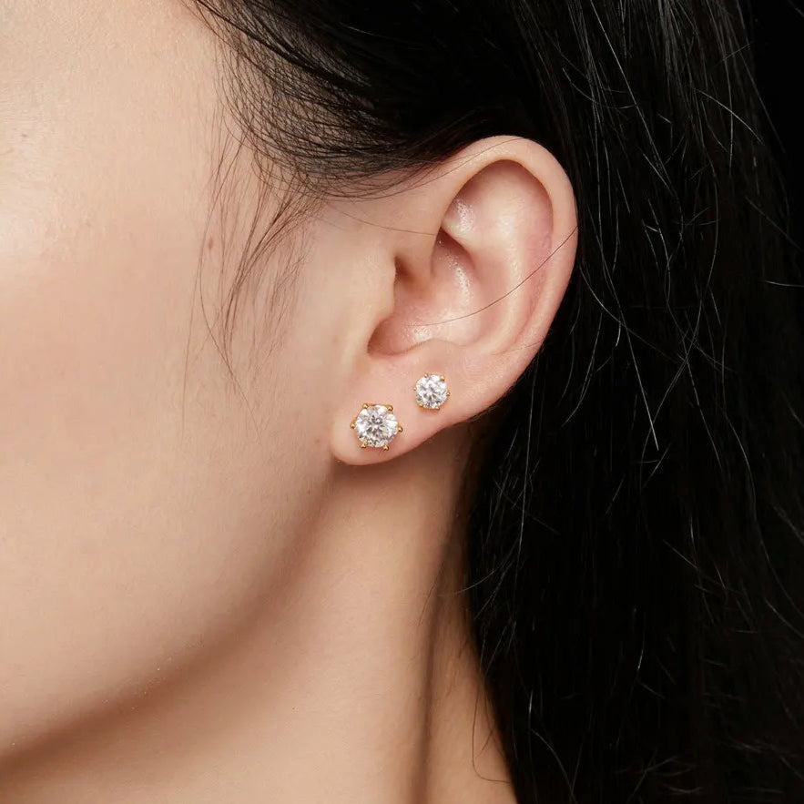 Close-up of an ear wearing diamond stud earrings with a soft focus background.