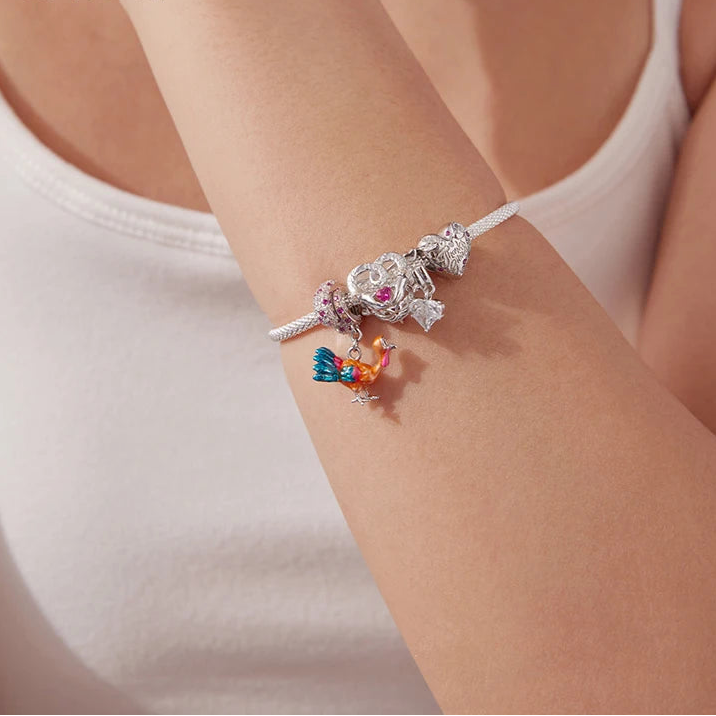 Silver bracelet with charms on a wrist, brand 'mirrorquenn' visible