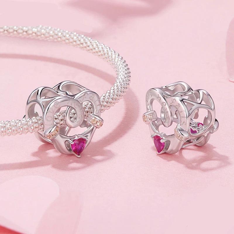 Silver heart-shaped jewelry with pink gemstones on a pink background, featuring the mirrorquenn brand.